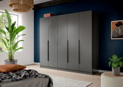 Moderner grauer Kleiderschrank mit vier Türen und langen schwarzen Griffen in einem Schlafzimmer vor dunkelblauer Wand, Perspektive: frontale Ansicht mit leichtem Blick von links.