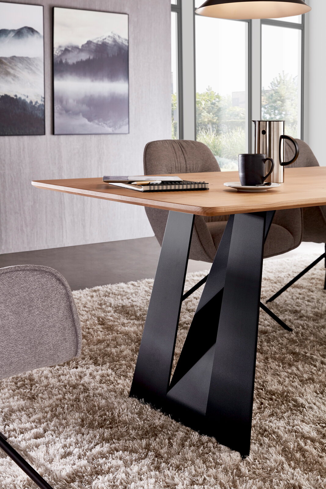 Moderner Esstisch mit heller Holzplatte und schwarzem V-förmigem Metallgestell, seitliche Perspektive im Wohn-/Essbereich mit Stühlen, Tasse und Kanne auf dem Tisch