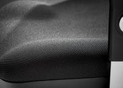 Nahaufnahme eines Drehsessels mit schwarzem, strukturiertem Stoffbezug und einem Teil der Armlehne.