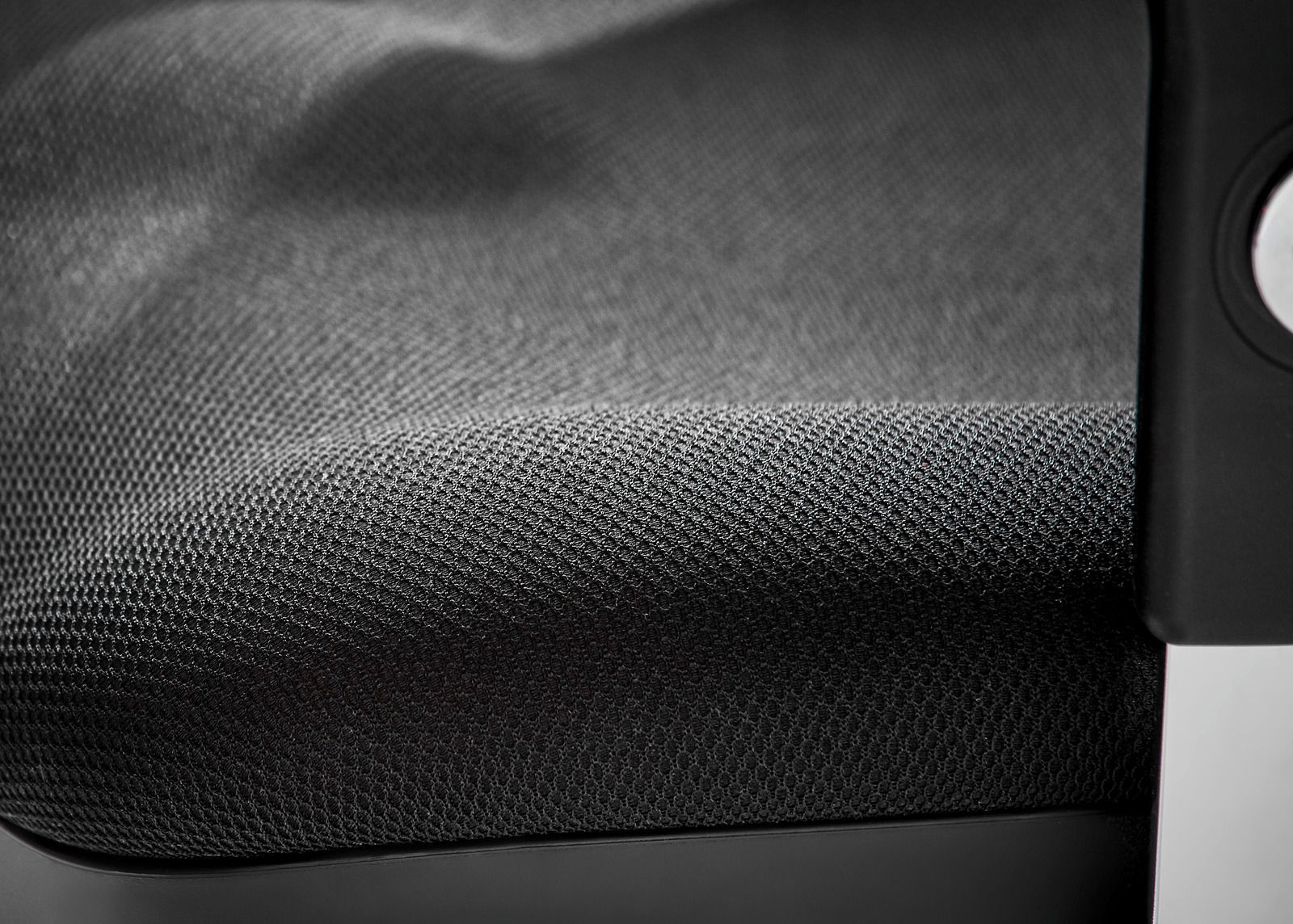 Nahaufnahme eines Drehsessels mit schwarzem, strukturiertem Stoffbezug und einem Teil der Armlehne.