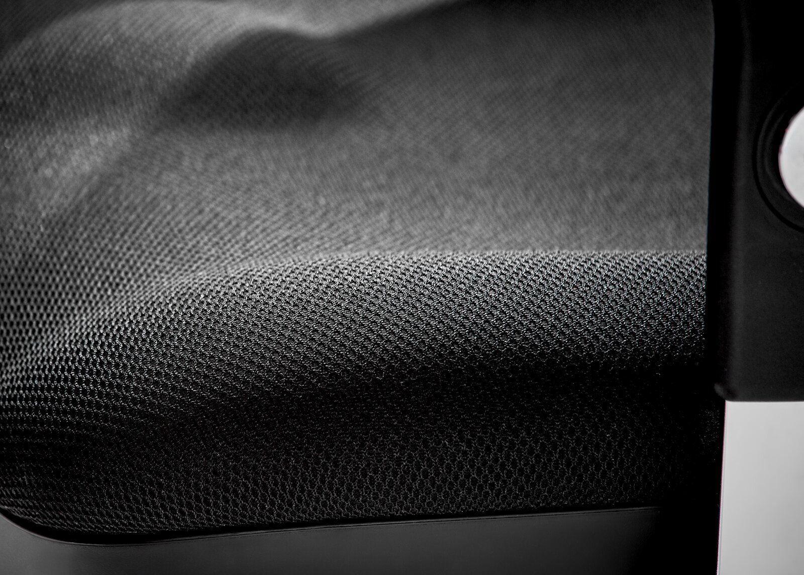 Nahaufnahme eines Drehsessels mit schwarzem, strukturiertem Stoffbezug und einem Teil der Armlehne.