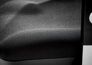 Nahaufnahme eines Drehsessels mit schwarzem, strukturiertem Stoffbezug und einem Teil der Armlehne.