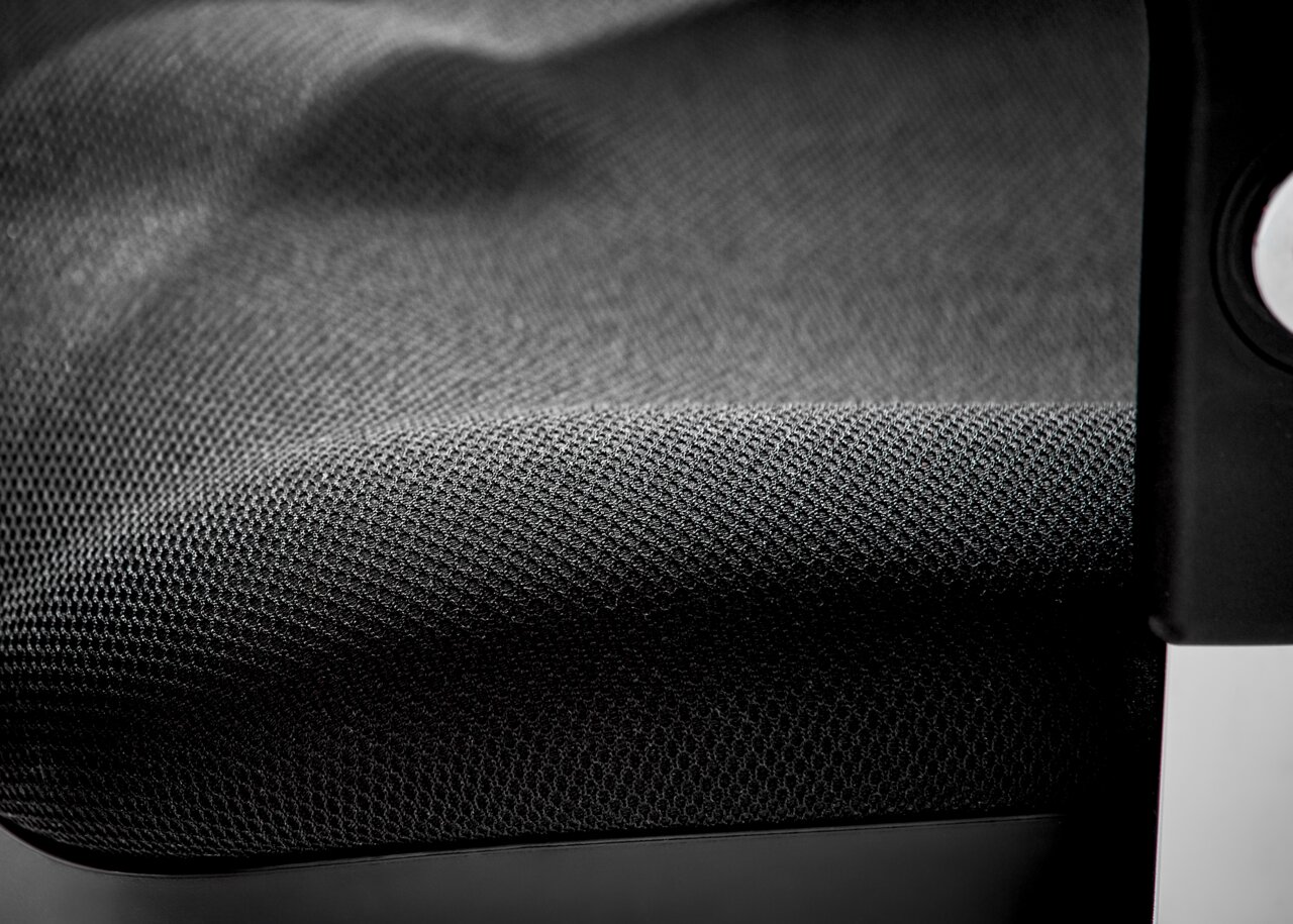 Nahaufnahme eines Drehsessels mit schwarzem, strukturiertem Stoffbezug und einem Teil der Armlehne.