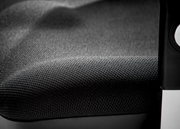 Nahaufnahme eines Drehsessels mit schwarzem, strukturiertem Stoffbezug und einem Teil der Armlehne.