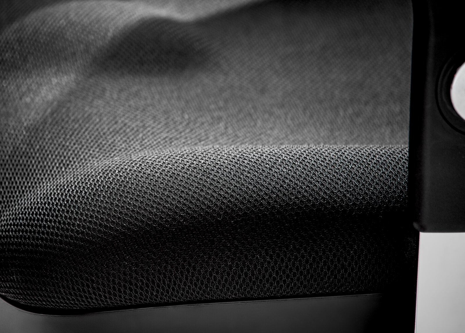 Close-up van een draaistoel met een zwarte, gestructureerde stoffen bekleding en een deel van de armleuning.