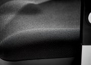 Close-up van een draaistoel met een zwarte, gestructureerde stoffen bekleding en een deel van de armleuning.