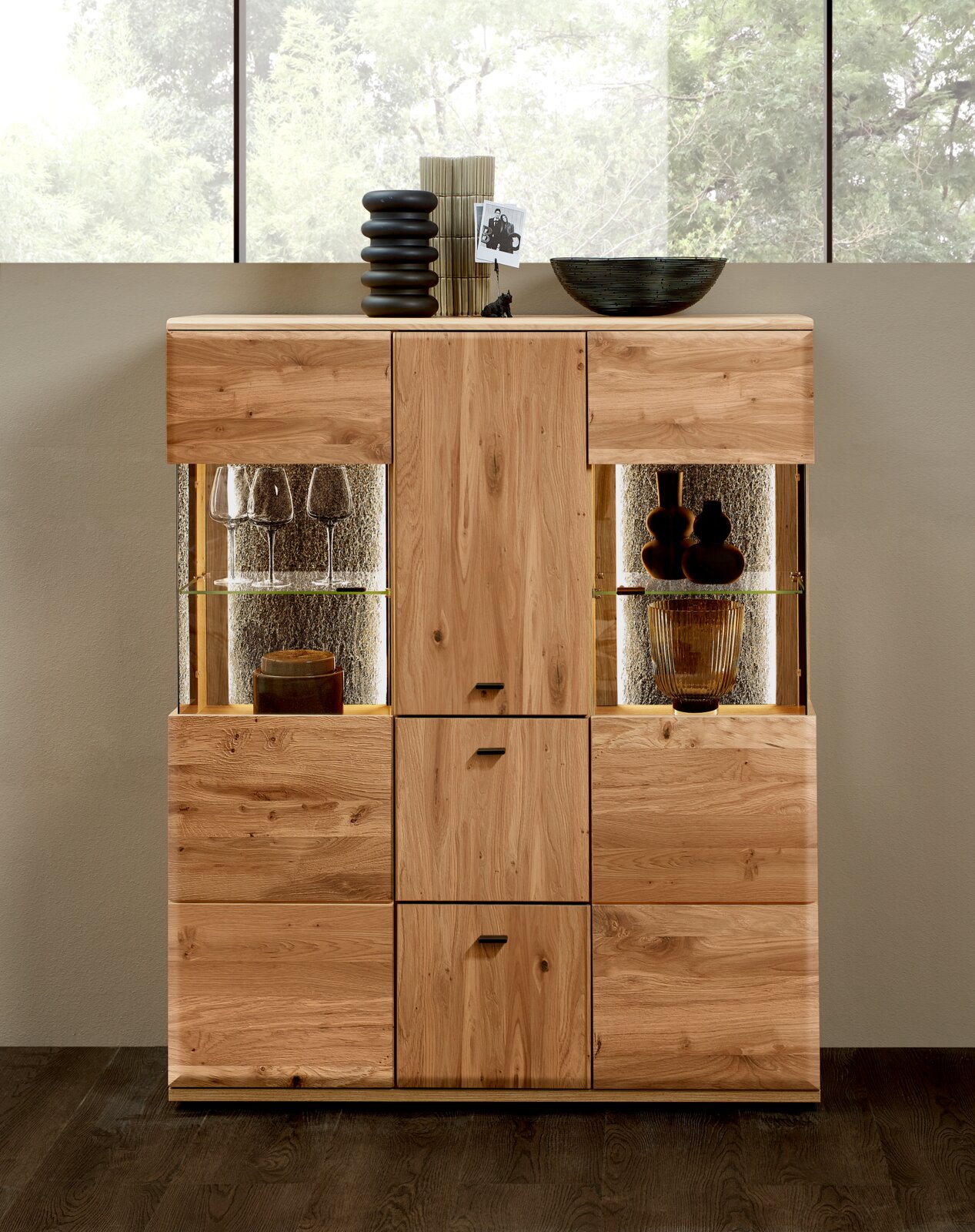 Massief houten vitrinekast/dressoir met twee verlichte glazen vakken en deuren, frontaal aanzicht, gestyled met glazen, vazen en decoratie op het blad.