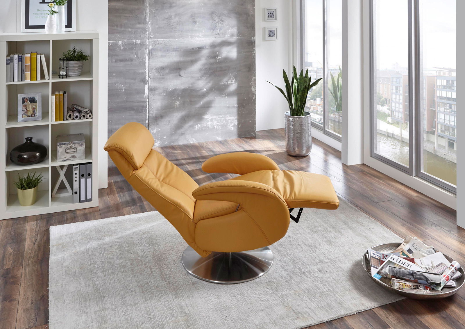 Moderner gelber Fernsehsessel in einem hellen Wohnzimmer mit großen Fenstern, seitliche Perspektive.