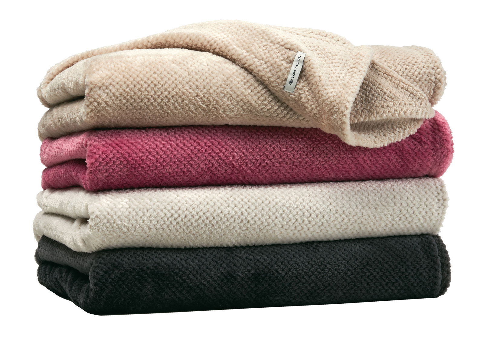 Gestapelte Plaids in verschiedenen Farben, von oben nach unten: Beige, Rot, Creme und Schwarz, aus seitlicher Perspektive fotografiert.