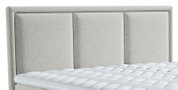 Lichtgrijs gestoffeerd bed met een hoog, driedelig gepolsterd hoofdbord en witte matras, schuin van voren afgebeeld