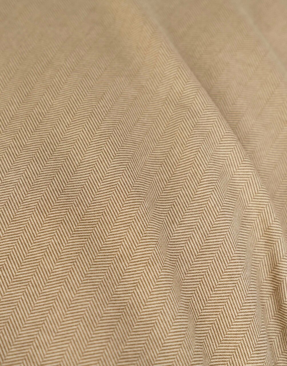 Nahaufnahme einer Bettwäsche mit Fischgrätenmuster in Beige, diagonale Perspektive
