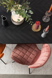 Vogelperspektive auf einen eleganten, rosafarbenen Stuhl mit gesteppter Polsterung neben einem Tisch mit Kerzen und Pflanzen.