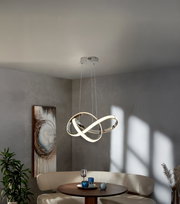Moderne LED-Pendelleuchte mit verschlungenen, ringförmigen Lichtbändern in Chromoptik über einem runden Esstisch in grauem Wohnraum, Ansicht leicht von unten (Untersicht)