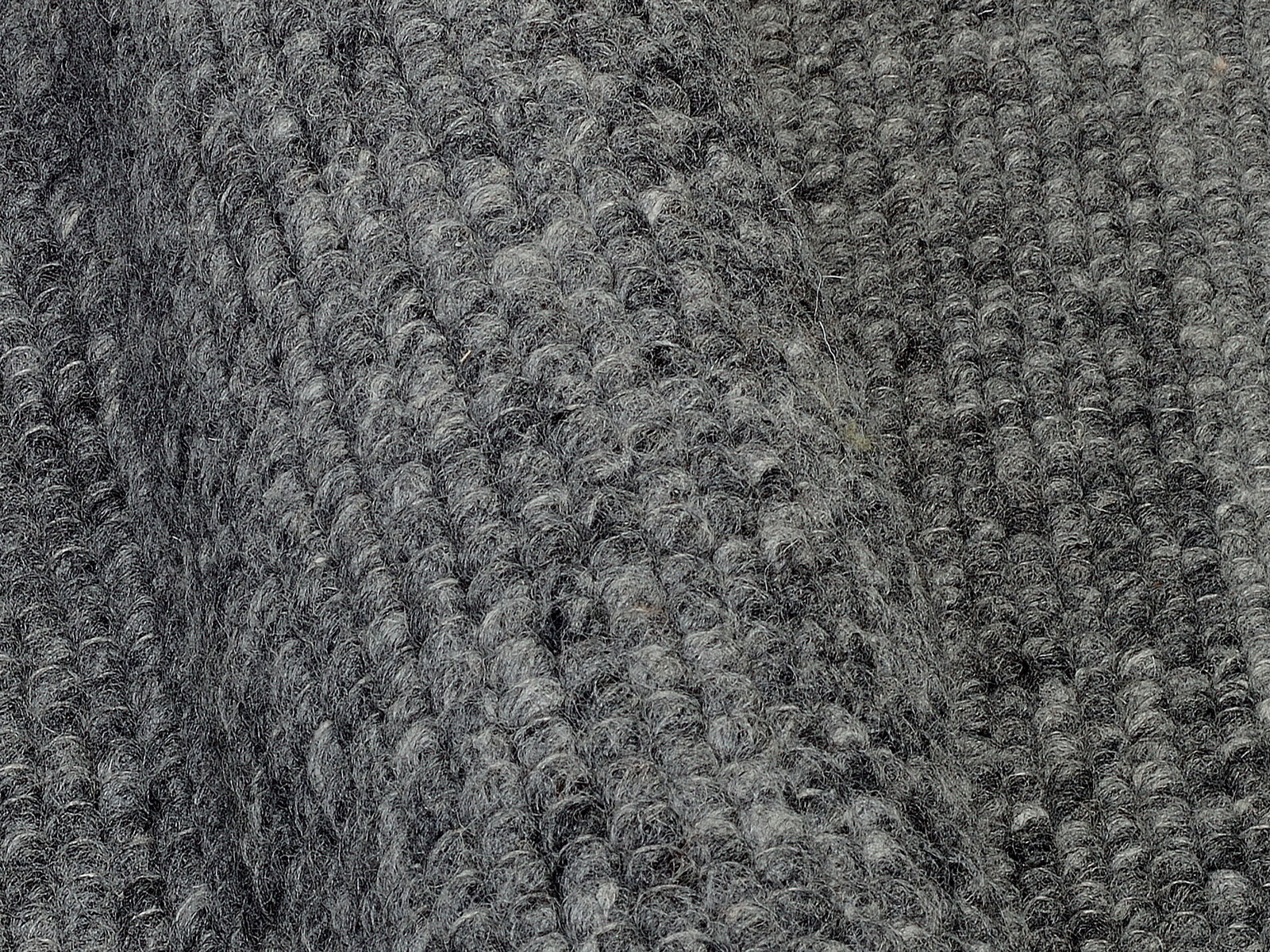 Nahaufnahme eines grauen Handweb Teppichs mit strukturierter Oberfläche, seitliche Perspektive