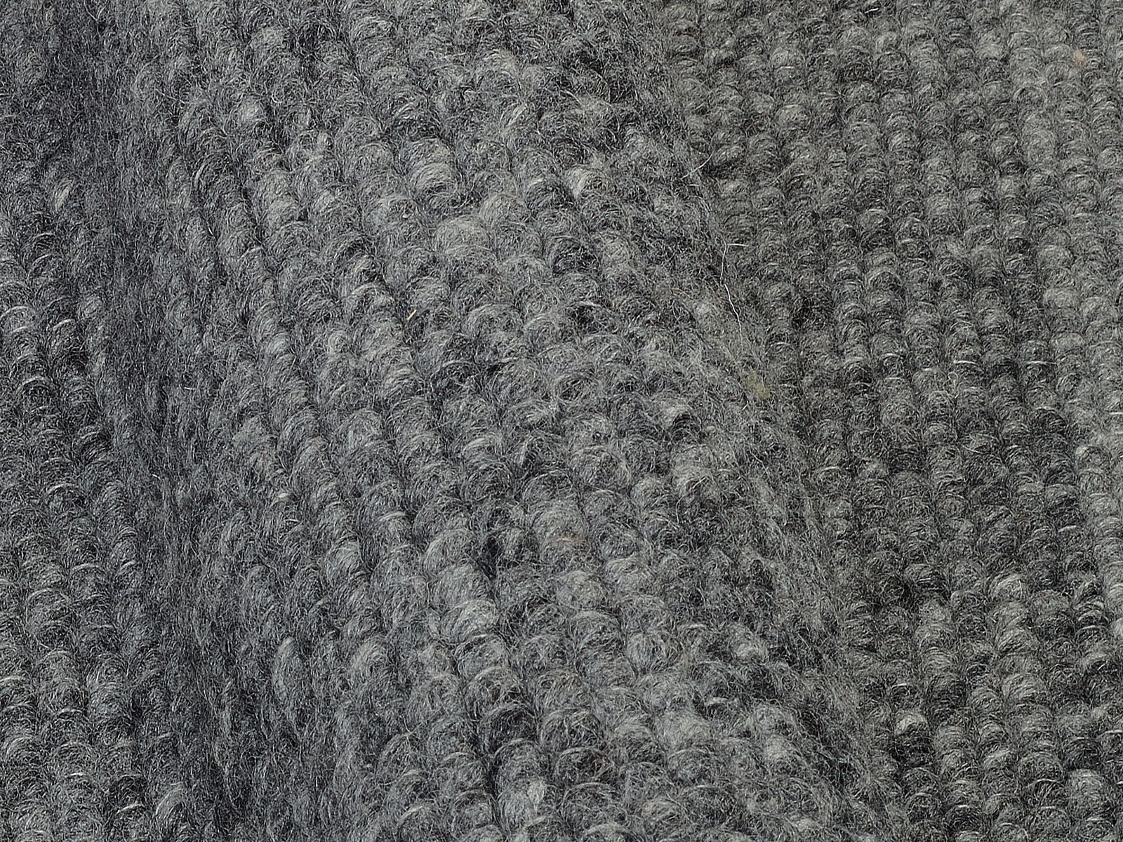 Nahaufnahme eines grauen Handweb Teppichs mit strukturierter Oberfläche, seitliche Perspektive