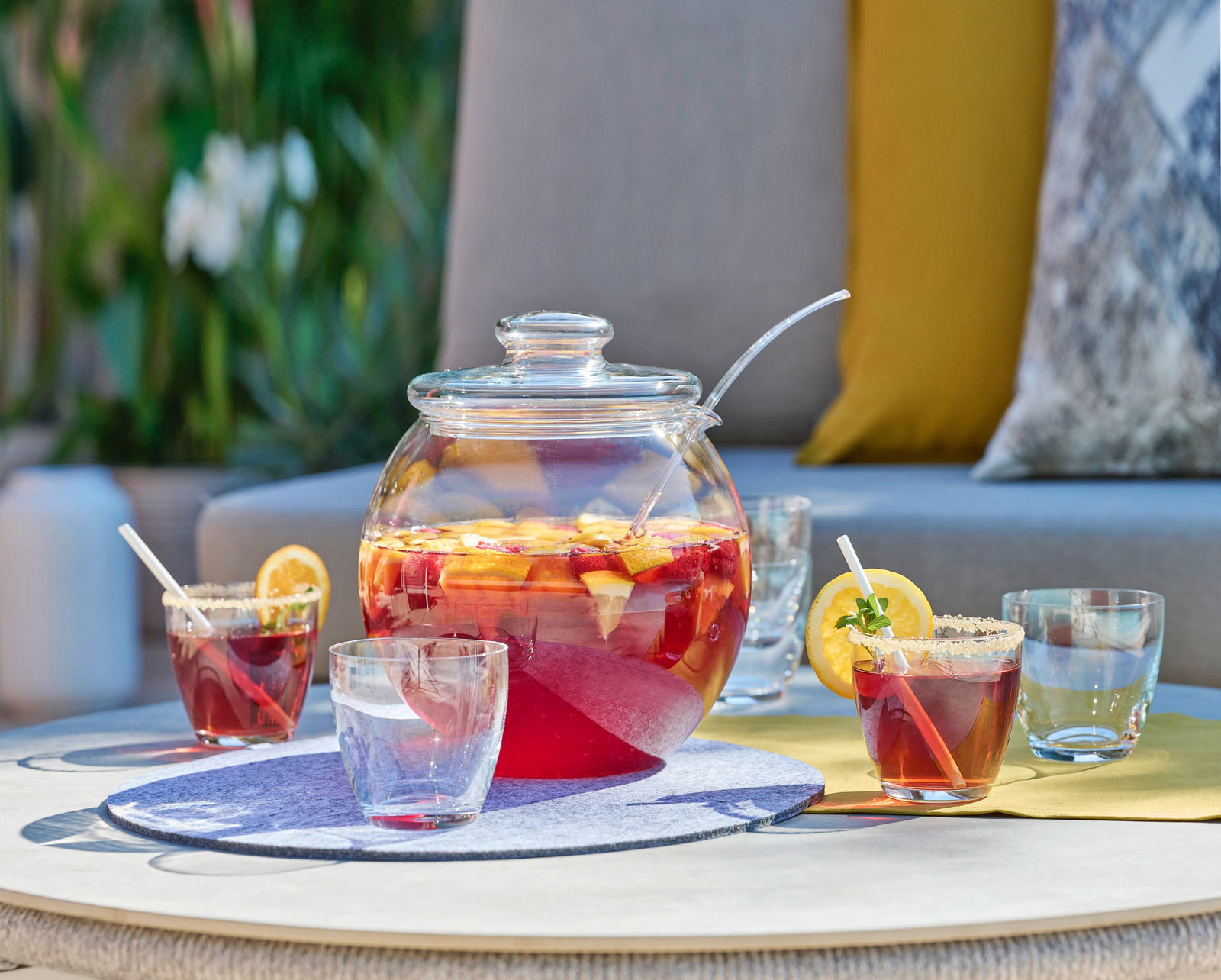 Bowle-Set mit Glaskrug und Gläsern, gefüllt mit fruchtiger Bowle, auf einem Tisch im Freien, seitliche Perspektive