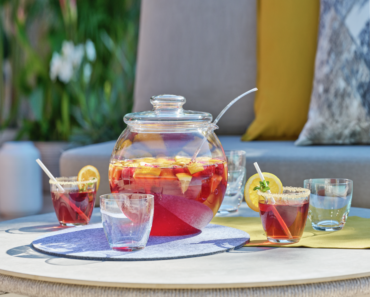 Bowle-Set mit Glaskrug und Gläsern, gefüllt mit fruchtiger Bowle, auf einem Tisch im Freien, seitliche Perspektive