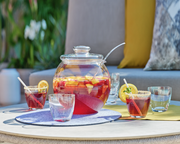 Bowle-Set mit Glaskrug und Gläsern, gefüllt mit fruchtiger Bowle, auf einem Tisch im Freien, seitliche Perspektive