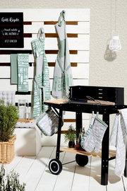 Küchen- und Grillzubehör-Set mit Geschirrtüchern, Schürzen und Topflappen in grün-weißem Design mit der Aufschrift 'Kiss the Cook', präsentiert neben einem Grill aus seitlicher Perspektive.