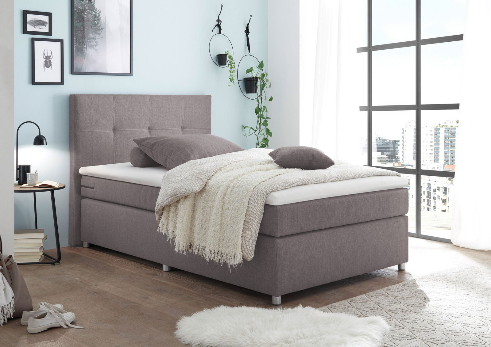 Modernes Boxspringbett in einem hellen Schlafzimmer mit großen Fenstern, seitliche Perspektive