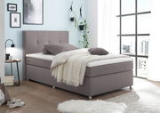 Modernes Boxspringbett in einem hellen Schlafzimmer mit großen Fenstern, seitliche Perspektive