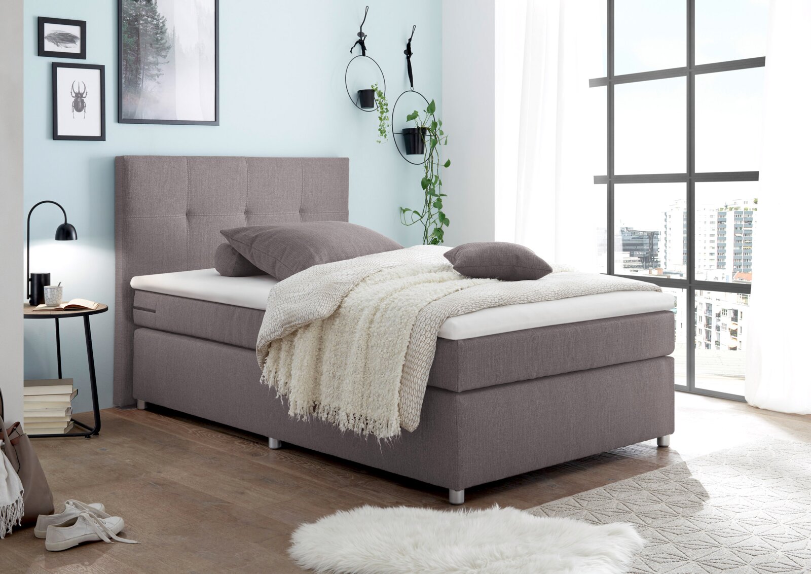 Modern boxspringbed in een lichte slaapkamer met grote ramen, zijaanzicht