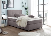 Modern boxspringbed in een lichte slaapkamer met grote ramen, zijaanzicht