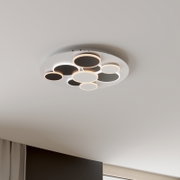 Moderne runde LED-Deckenleuchte mit mehreren kreisförmigen Leuchtringen in Weiß und Schwarz, montiert an der Decke; Perspektive von unten leicht seitlich (Untersicht).