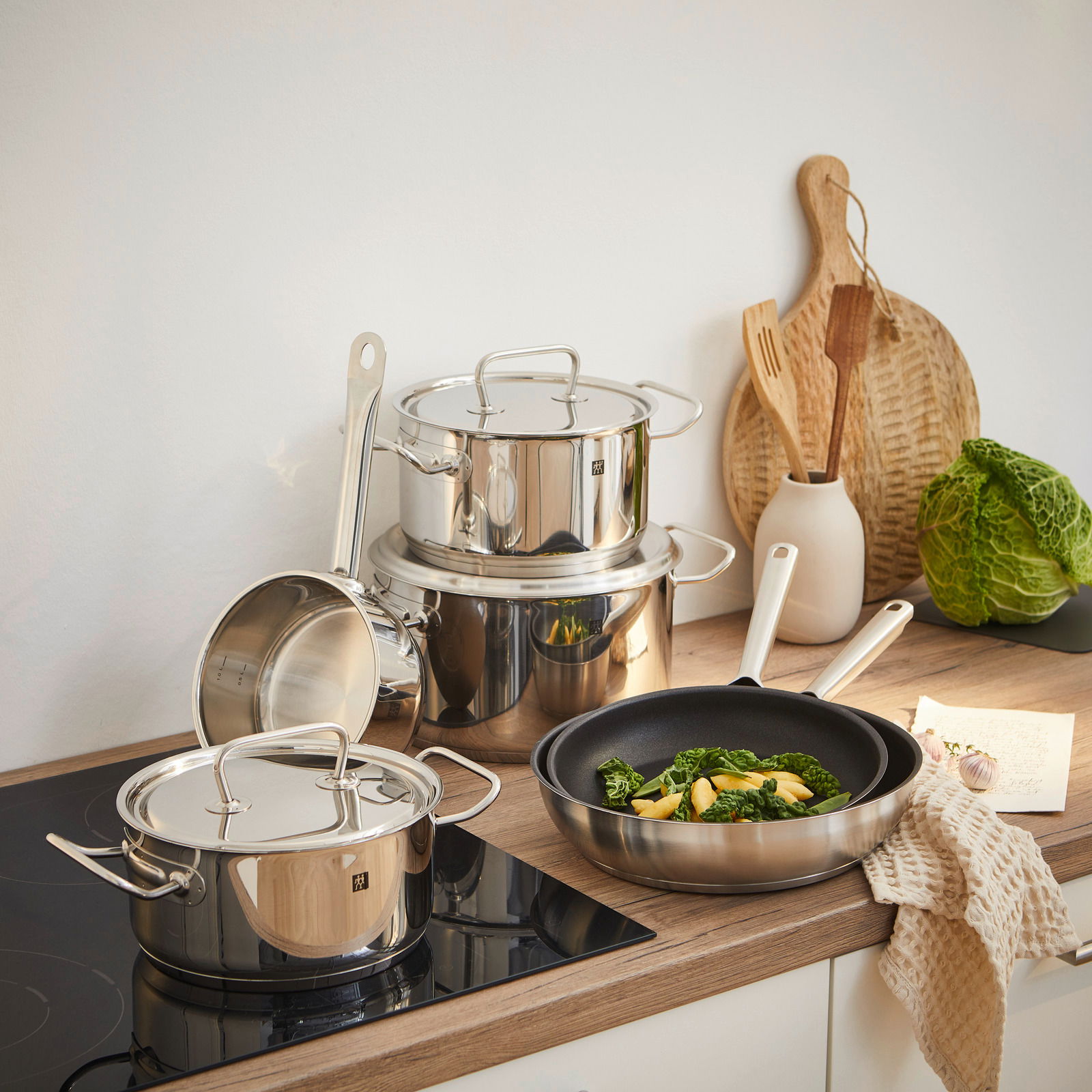 Küchenansicht mit einem sechsteiligen Topfset Twin Classic aus Edelstahl, bestehend aus Töpfen und Pfannen, auf einem Herd und einer Arbeitsplatte arrangiert.