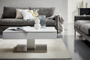 Moderner weißer Couchtisch in einem stilvollen Wohnzimmer, frontal fotografiert, mit grauem Sofa im Hintergrund und dekorativen Elementen auf dem Tisch.