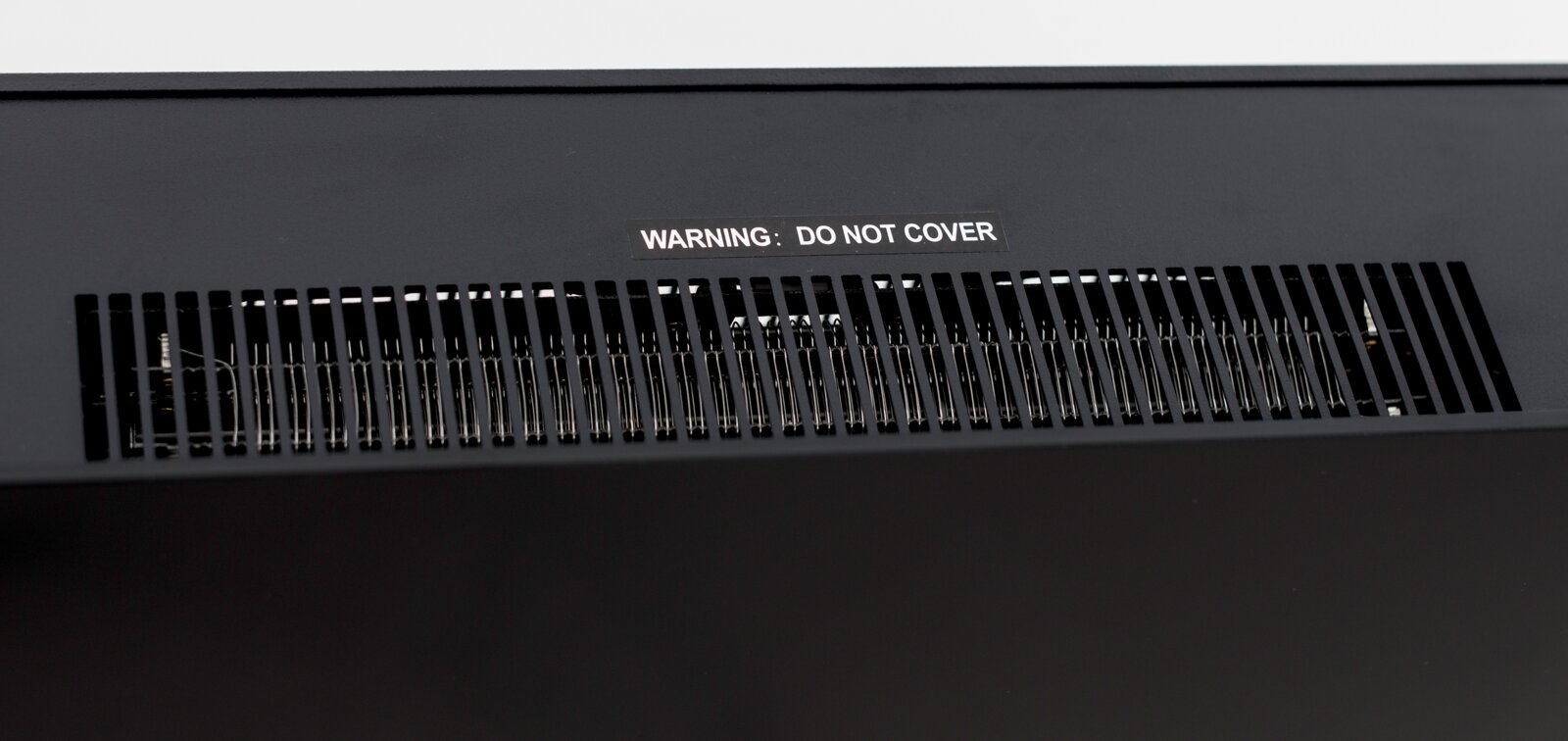 Nahaufnahme der Lüftungsschlitze eines Elektrokamins mit Warnhinweis 'DO NOT COVER'.