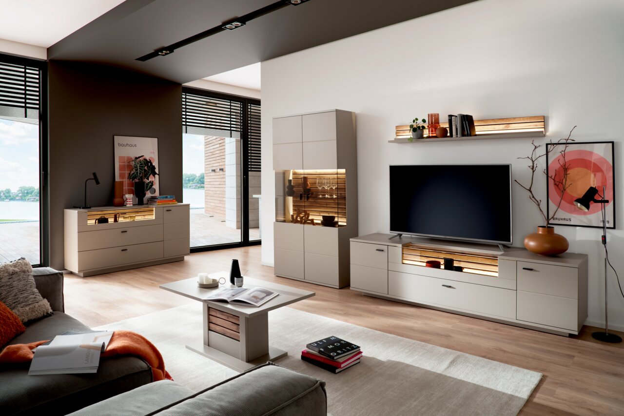 Moderne Wohnzimmermöbel mit Sideboard, Highboard, Wandboard und Esstisch in einem hellen Raum mit großen Fenstern, seitliche Perspektive.