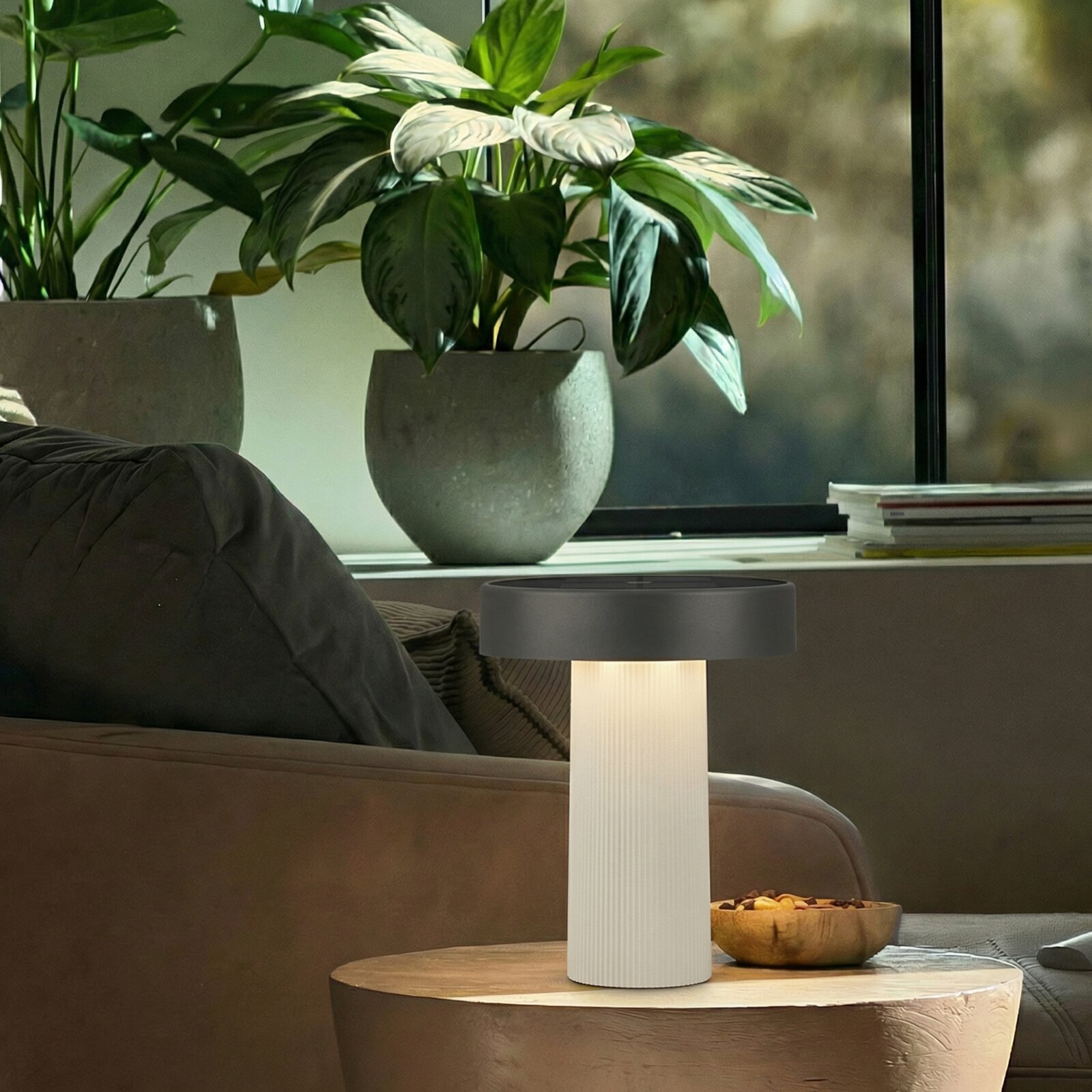 Moderne Tischlampe mit weiß geriffeltem Zylinderfuß und dunkelgrauem, flachem Lampenschirm auf rundem Holz-Couchtisch im Wohnzimmer, Perspektive: frontale leicht erhöhte Ansicht
