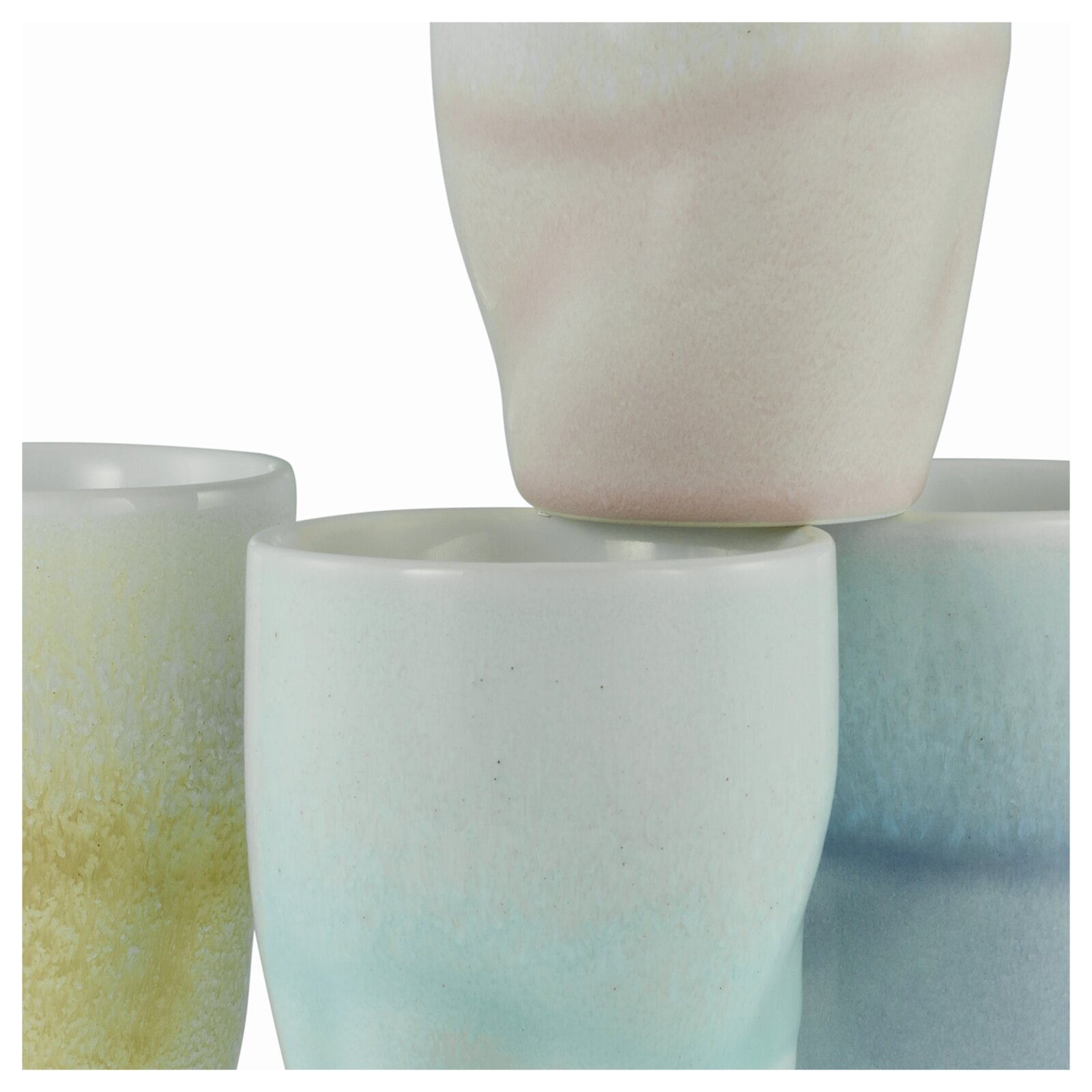 Stapel aus glasierten Keramikbechern in Pastellfarben (Gelb, Mint, Blau und Rosé) vor weißem Hintergrund, Nahaufnahme aus leicht seitlicher Perspektive.