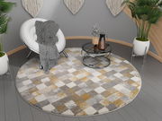 Runder Frisé-Teppich mit geometrischem Muster in Grau-, Weiß- und Gelbtönen, auf einem modernen grauen Boden in einem stilvoll eingerichteten Raum mit Pflanzen und einem Sessel, aus der Vogelperspektive betrachtet.