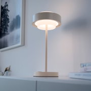 Moderne weiße Tischlampe mit rundem Schirm und warmem Licht auf einem Sideboard, fotografiert in leichter Untersicht von vorn in einem hellen Wohnraum