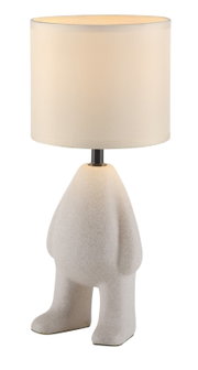 Vooraanzicht van een decoratieve tafellamp met een cilindervormige, crèmekleurige stoffen kap en een sculpturale, wit gespikkelde voet in de vorm van een figuur, op een witte achtergrond