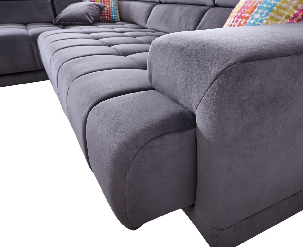 Graue Polsterrundecke in Nahaufnahme, Perspektive von der Seite mit bunten Kissen im Hintergrund.