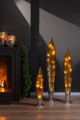 Drei moderne, goldene Kerzenhalter in Blattform mit Teelichtern, stehend auf einem Holzfußboden vor einer dunklen Wand. Perspektive: Frontalansicht.