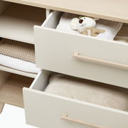 Kommode mit zwei offenen Schubladen, gefüllt mit einem Stofftier und Textilien, aus einer schrägen Perspektive fotografiert.