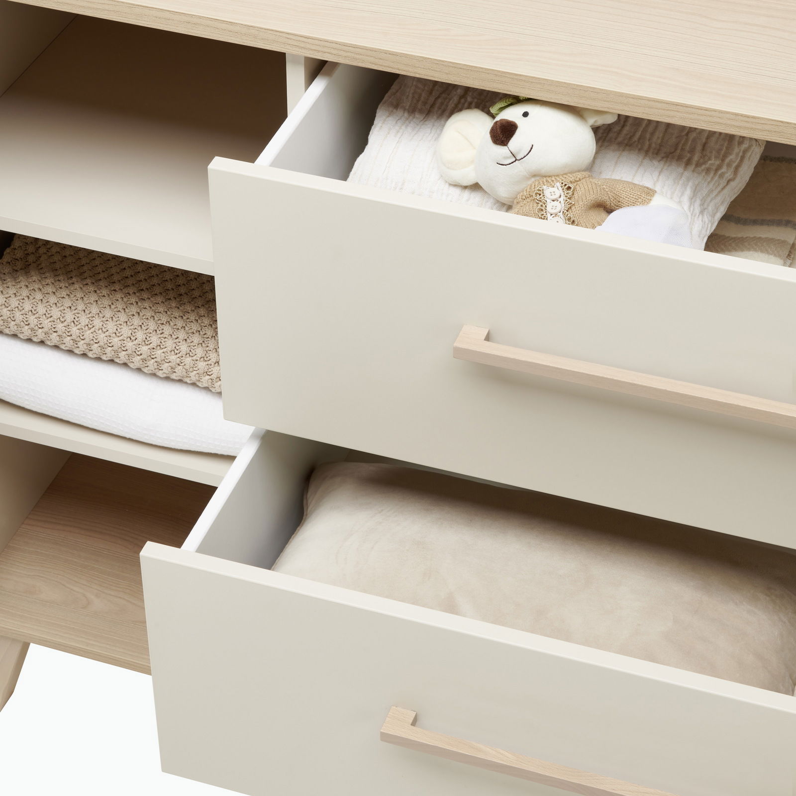 Kommode mit zwei offenen Schubladen, gefüllt mit einem Stofftier und Textilien, aus einer schrägen Perspektive fotografiert.