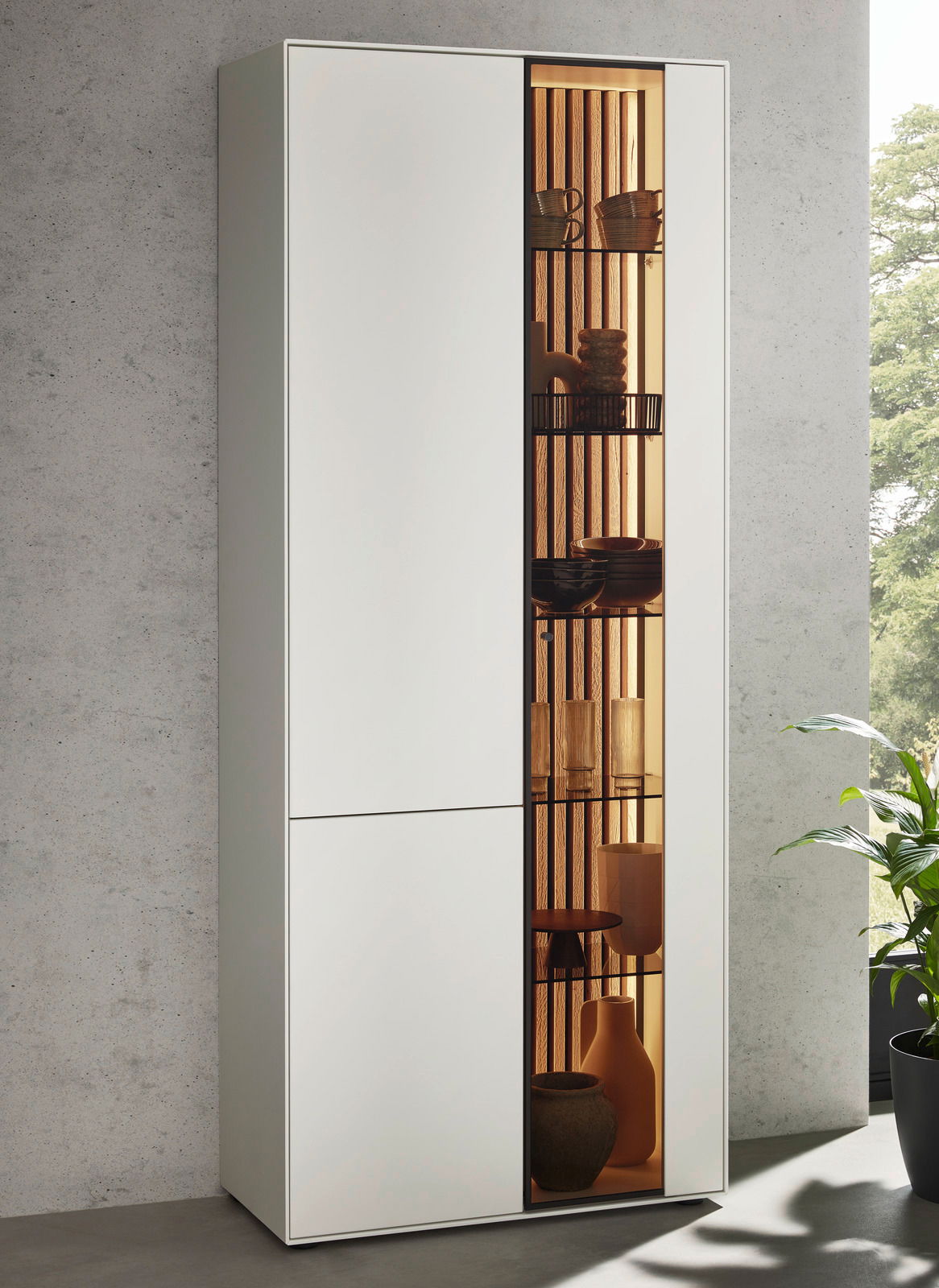 Moderne Standvitrine LUCIANO mit linksseitiger Tür und rechtsseitigem Glaseinsatz, frontal betrachtet, mit dekorativer Beleuchtung und stilvollen Accessoires.