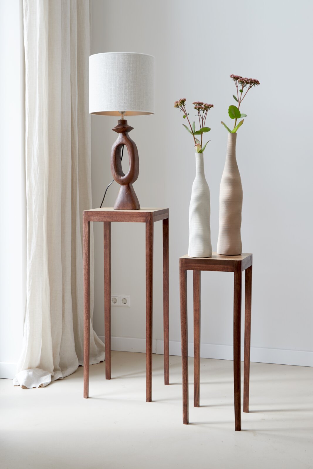 Moderne cilindervormige lampenkap 35-35-30 op een kunstig bewerkte houten voet, zijaanzicht, naast twee hoge vazen op een houten tafel.