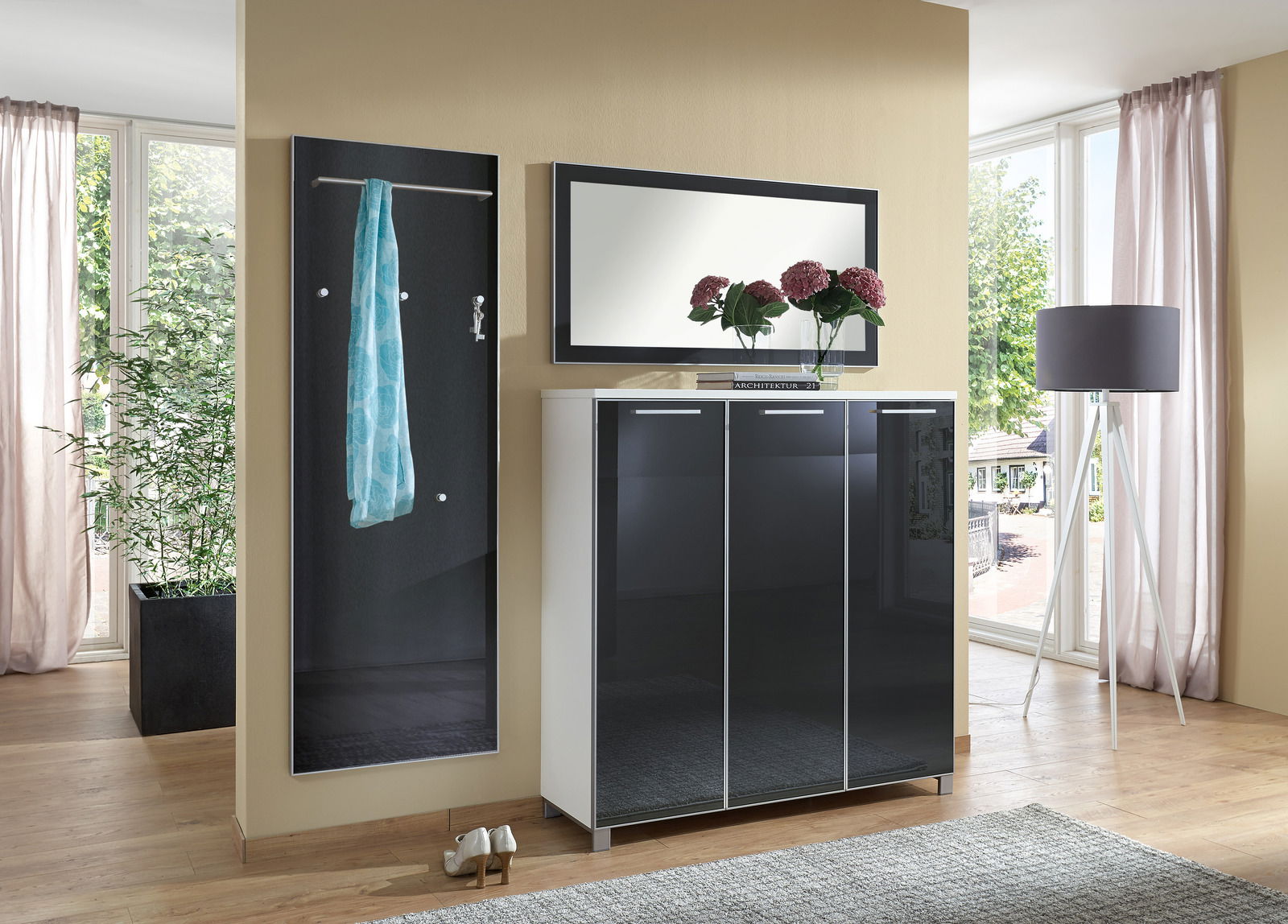 Modernes Garderoben-Set bestehend aus einem schwarzen Wandpaneel mit Kleiderstange, einem Spiegel und einem dreitürigen Schrank in Hochglanzoptik. Perspektive: Frontalansicht.