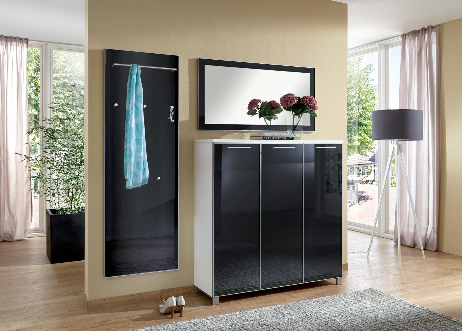 Modernes Garderoben-Set bestehend aus einem schwarzen Wandpaneel mit Kleiderstange, einem Spiegel und einem dreitürigen Schrank in Hochglanzoptik. Perspektive: Frontalansicht.
