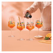 Vier bunte Weingläser mit Fruchtmotiven, gefüllt mit einem orangen Getränk, auf einem Tisch. Eine Hand gießt ein Getränk in eines der Gläser. Perspektive von vorne.