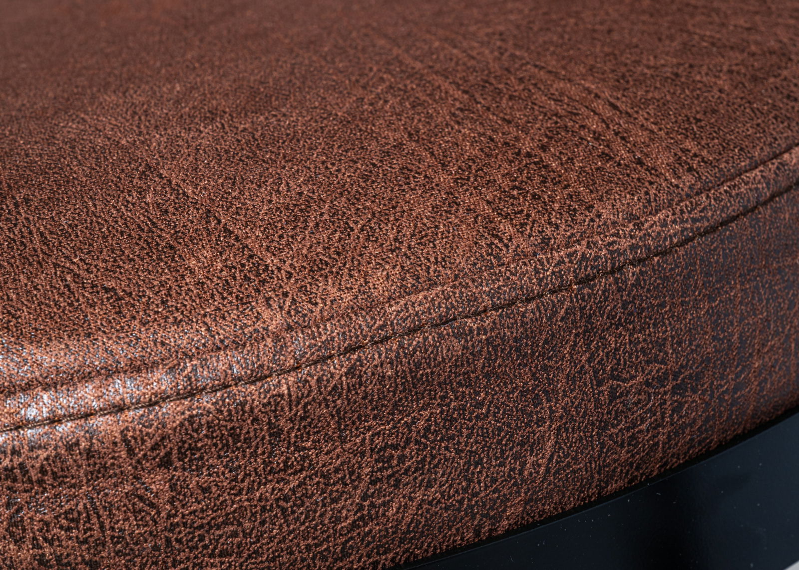 Nahaufnahme eines braunen Drehstuhlsitzes mit strukturierter Oberfläche, seitliche Perspektive