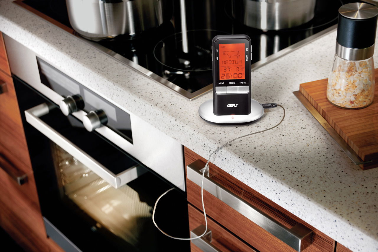 Digitales Bratenthermometer auf einer Küchenarbeitsplatte neben einem Herd, seitliche Perspektive