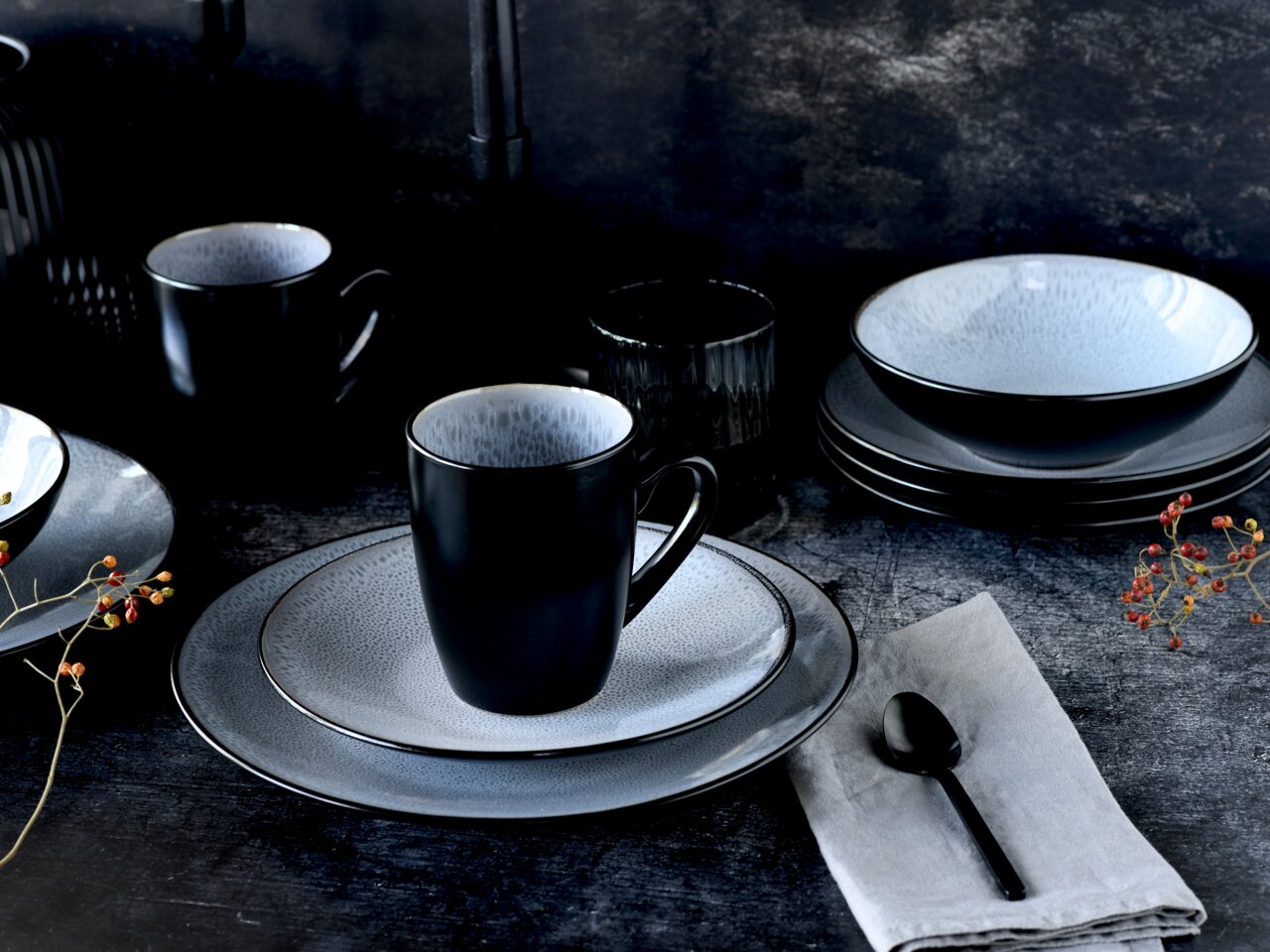 Elegantes Kombiservice 16-tlg in Schwarz und Grau, bestehend aus Tellern, Schalen und Tassen, auf einem dunklen Tisch arrangiert. Seitliche Perspektive.