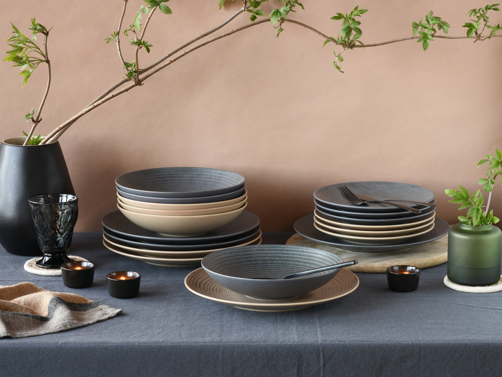 Elegantes 18-teiliges Tellerset in Schwarz und Beige, präsentiert auf einem gedeckten Tisch mit dekorativen Elementen, aus seitlicher Perspektive fotografiert.